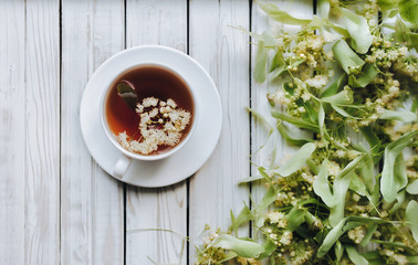 White cup of linden tea on linden blossom background. Herbal medicine. Top view. Treatment of cold and flu concept. Concept of prevention coronavirus COVID-19.