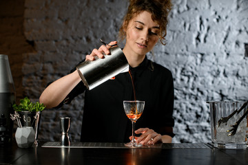 Lady bartender pours ready-made cocktail into glass.