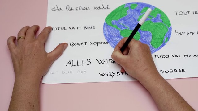 Hands write all will be ok in many languages around a colored earth. Zoom in