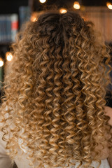 Closeup view vertical photography of amazing beautiful long curly female hair style made in professional beauty spa salon.