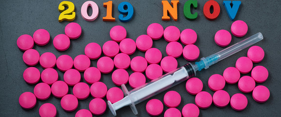 The name of the Chinese flu, its abbreviation. Pink pills and a syringe are scattered on a gray background. The concept of treatment of influenza.