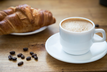 
White cup with latte coffee and croissant on a wooden table