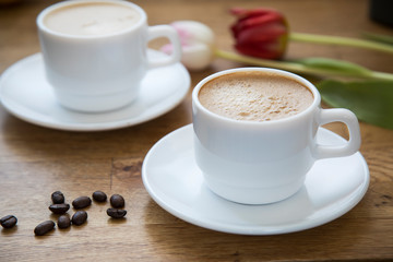 
Two white cups with latte coffee and flowers on a wooden table
