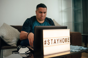  hashtag stay home. young  hispanic man sitting on couch and working at his laptop during quarantine.