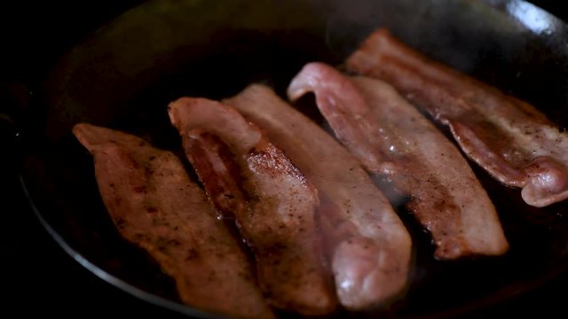Streaky Bacon frying in black cast iron skillet