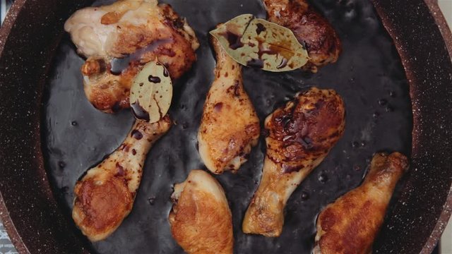 Soy sauce and bay leaves bubbling and steaming as it is poured into a brown rustic pan with roasted chicken pieces. Top View.