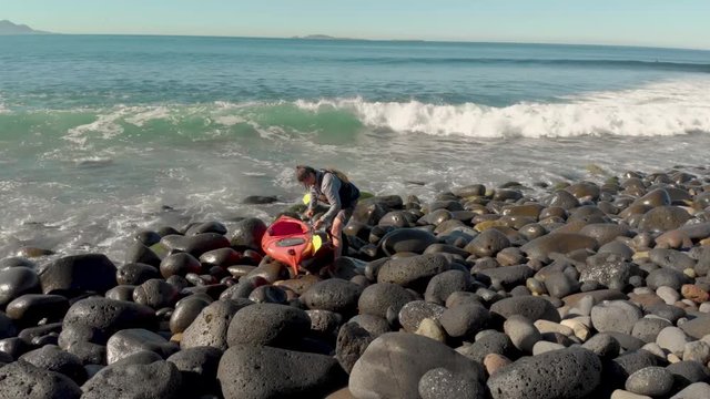 A kayaker entering the ocean from a rocky beach.
