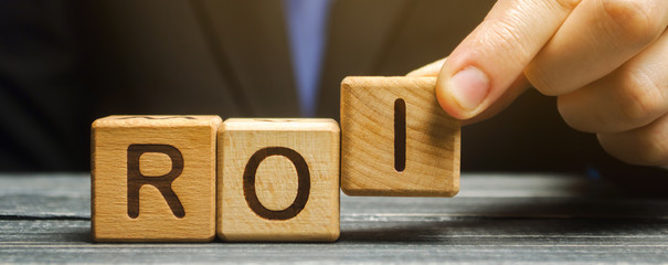 Businessman puts wooden blocks with the word ROI. Return on investment concept. Profitability and...