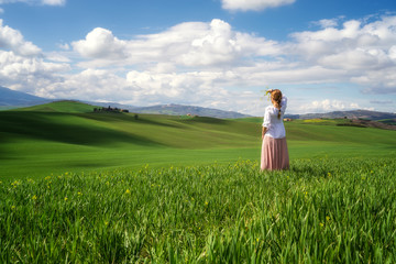 Fototapeta na wymiar Rear view of a woman with vintage clothes admires the beauty of green rolling hills in the heart of Tuscany, Italy.