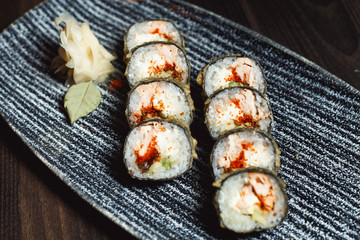 Top view assorted sushi set on a black on plate, dark background. Japanese classic seafood, nigiri, rolls, soy sauce, ginger, copy space.