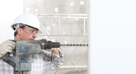 man using an electric pneumatic drill making a hole in wall, professional construction worker with...