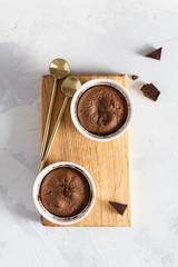Obraz na płótnie Canvas Delicious french fondant with hot chocolate in ramekins on wooden board. Lava cake recipe, menu. Top view