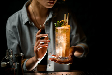 close-up of beautiful cocktail with ice which holds young woman at bar