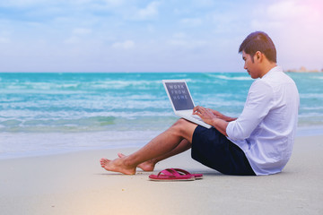 Happiness Handsome man with a shirt working with laptop sitting on the beach beside the sea. Working from home concept
