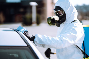 Hand of Man in protective suit washing and disinfection handles of a car, to preventing the spread of the epidemic of coronavirus, pandemic in quarantine city. 