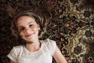 Fototapeta premium Smiling girl laying on the floor on a Persian carpet in a white dress.