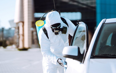 Man in protective suit washing and disinfection handles of a car, to preventing the spread of the...