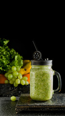 Fruits and greens smoothies in Mason jar. Behind are the fruits in a dark box on black background. Steampunk style, space for text, vertical format