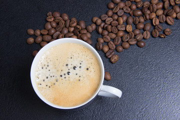cup of espresso and cofee seeds on black background top view