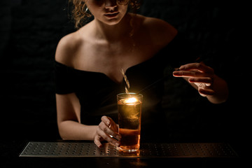 attractive sexy girl at bar decorates glass with alcoholic drink by spikelet.