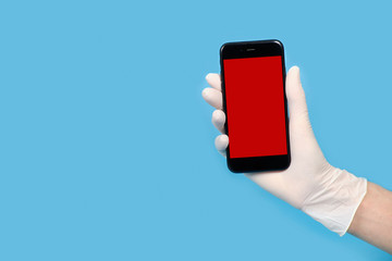 Hand in glove holds phone isolated on a blue background. place for text
