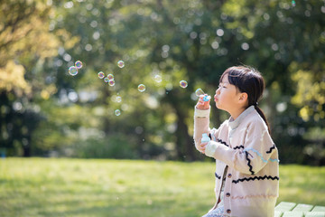 春の公園でシャボン玉を遊んでいる子供