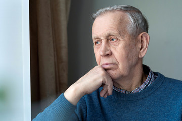 Portrait of senior man. A thoughtful, elderly man looks out of the window, sitting at home.