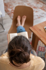 Fototapeta premium young lady evaluating the quarantine having a good time reading a book by stretching her feet at her home
