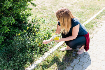 Young woman picking wild flowers by the sidewalk