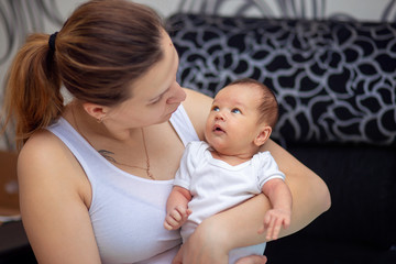 A young mother holds in her arms her newborn baby. Mom and baby look at each other
