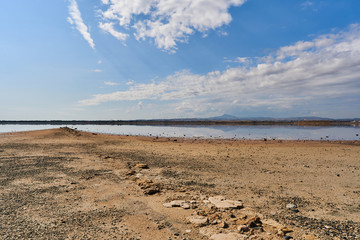 Beautiful panoramic view of a mountain from the shore of the salty lake Larnaca with blue sky and small clouds, reflections in the water, Larnaca, island Cyprus, deserted landscape