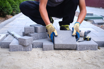 The master in yellow gloves lays paving stones in layers. Garden brick pathway paving by...