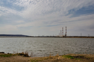 Fototapeta na wymiar Landscape, four pipes of a power plant on the shore of a reservoir in a spring cloudy day, against a blue sky with clouds.