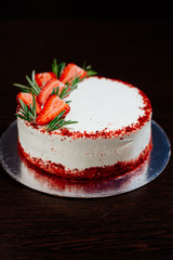 Red velvet cake on a dark background. Red velvet cake in white butter cream decorated with strawberry pieces and a sprig of rosemary. Red velvet cake in the cut.