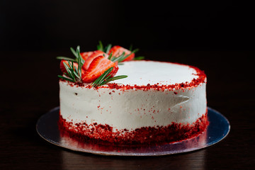 Red velvet cake on a dark background. Red velvet cake in white butter cream decorated with strawberry pieces and a sprig of rosemary. Red velvet cake in the cut.