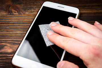 Cleaning phone screen to apply protective tempered glass on dark wooden background.