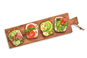 Open sandwiches with vegetables, avocado, tomato, mozzarella, boiled egg and soft cheese. Homemade sandwich with ham, cucumber, radish sprouts, herbs on wooden board isolated on white, top view