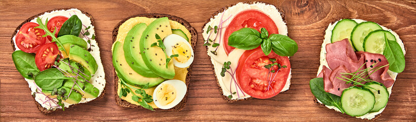 Open sandwiches with avocado, tomato, mozzarella and soft cheese. Homemade sandwich with ham, cucumber, radish sprouts on wooden board. Top view, sandwich closeup, banner