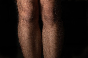 Fototapeta na wymiar Young male hairy legs closeup with dramatic shadows and black background