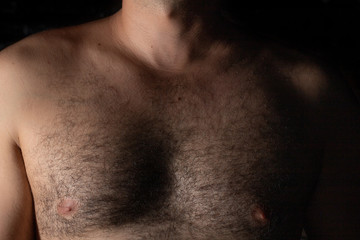 Young male hairy chest closeup with dramatic shadows and black background