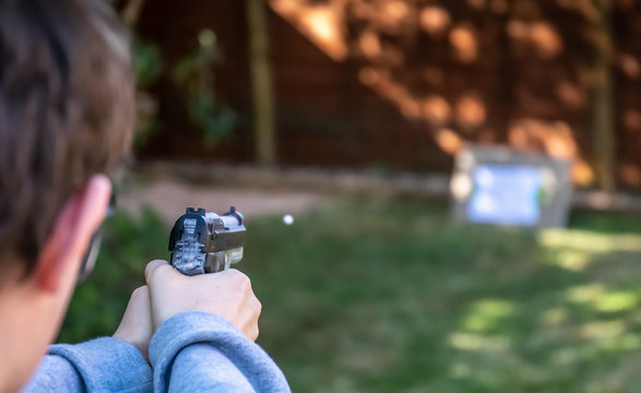 boy shoots white plastic bb pellet at target in garden with electric airsoft pistol