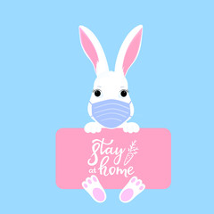 Funny Easter bunny in a medical mask holds in paws a sign with the inscription Stay home . Quarantine. Self isolation.