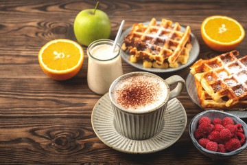 Belgian waffles, coffee, yogurt, fruits and berries on a wooden background, breakfast concept.