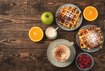 Obraz na płótnie Canvas Belgian waffles, coffee, yogurt, fruits and berries on a wooden background, breakfast concept.