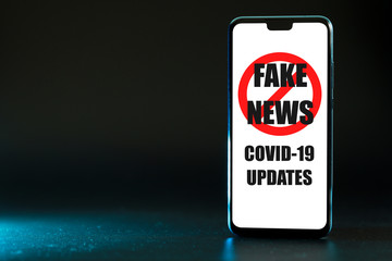 Smartphone with Stop Fake News of COVID-19 Updates text and symbol on the display screen, isolated on black background.