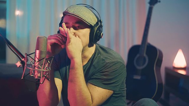 Musician in headphones playing on harmonica at home sitting on floor at evening time. Music hobby, Create own songs, learning online. 4K video
