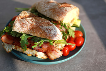 Fresh baguette sandwich with bacon, fried egg, parsley and grilled cherry tomatoes.