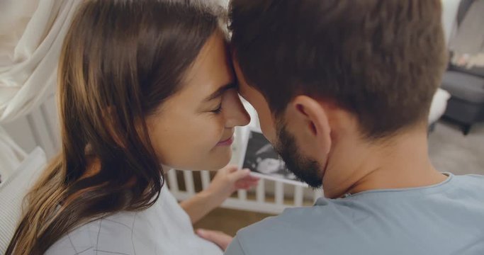 Pregnant woman and her husband with sonogram picture in nursery