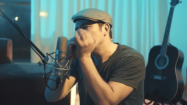 Musician in headphones playing on harmonica at home sitting on floor at evening time. Music hobby, Create own songs, learning online. 4K video
