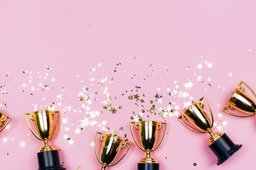 Golden winner cups with sparkles on a pink background with copy space. Festive concept. Flat lay style.
